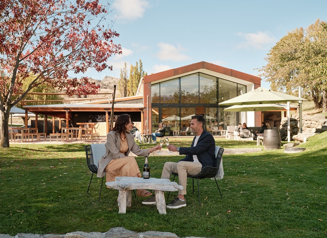 Two guests enjoying Pelorus Vintage lakeside with The Cloudy Bay Shed behind them