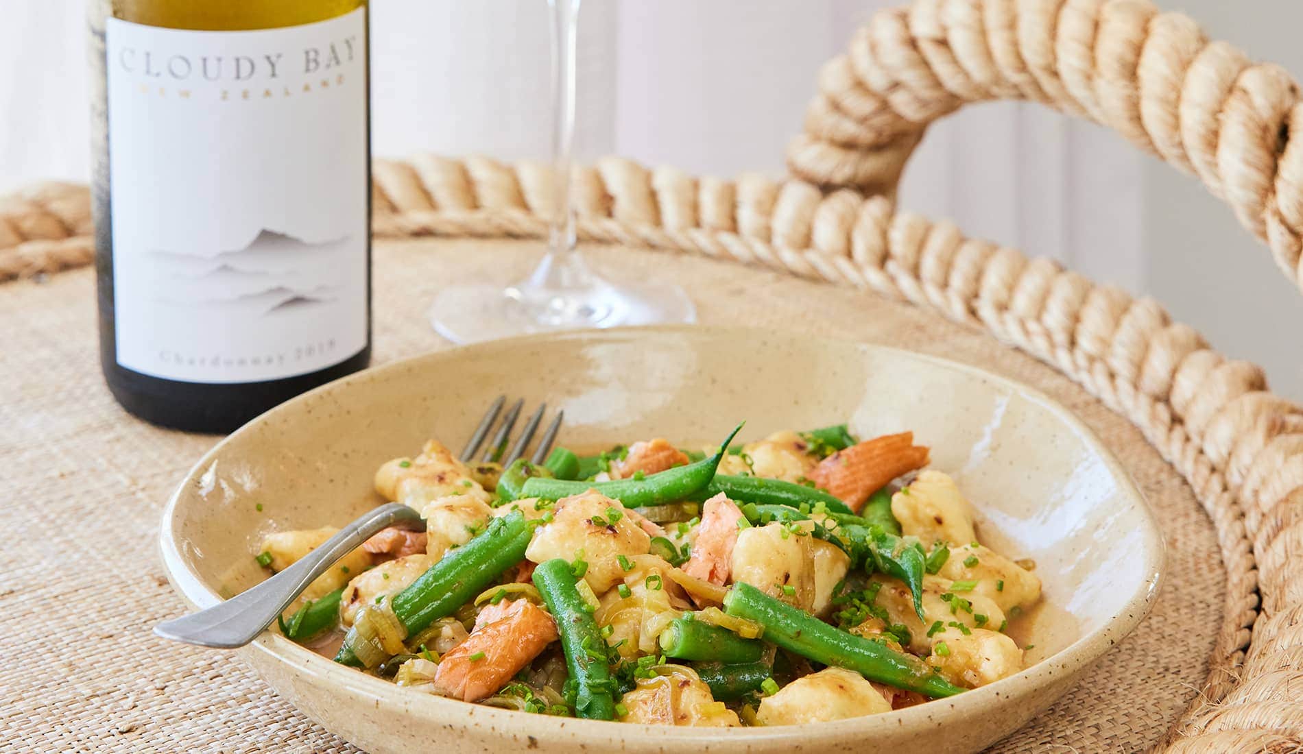Bowl of food beside bottle and glass of Cloudy Bay Chardonnay