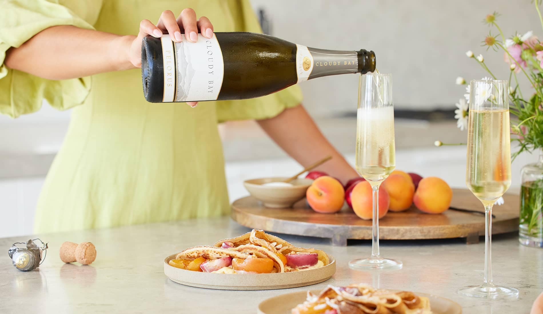 Person pouring a glass of Cloudy Bay Pelorus near two plates of pancakes