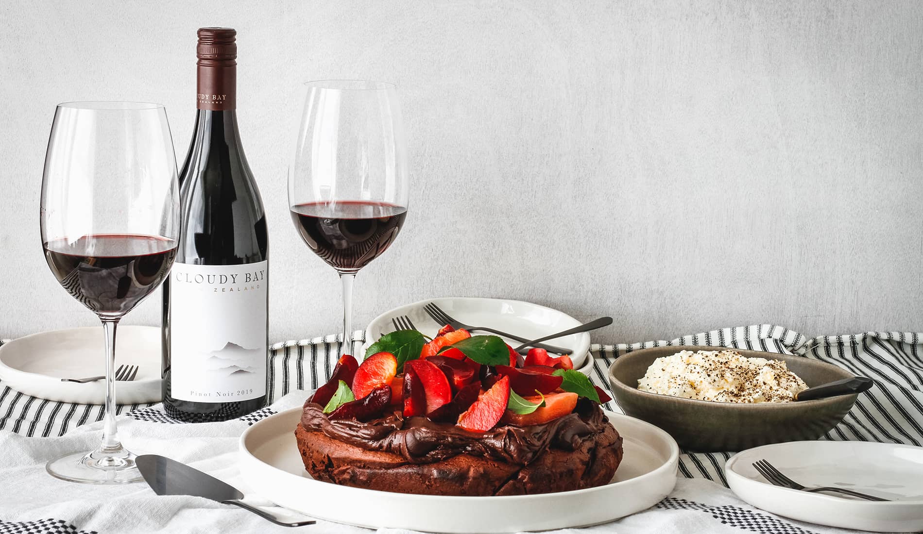 Chocolate cake with fruit beside bottle and glasses of Cloudy Bay Pinot Noir