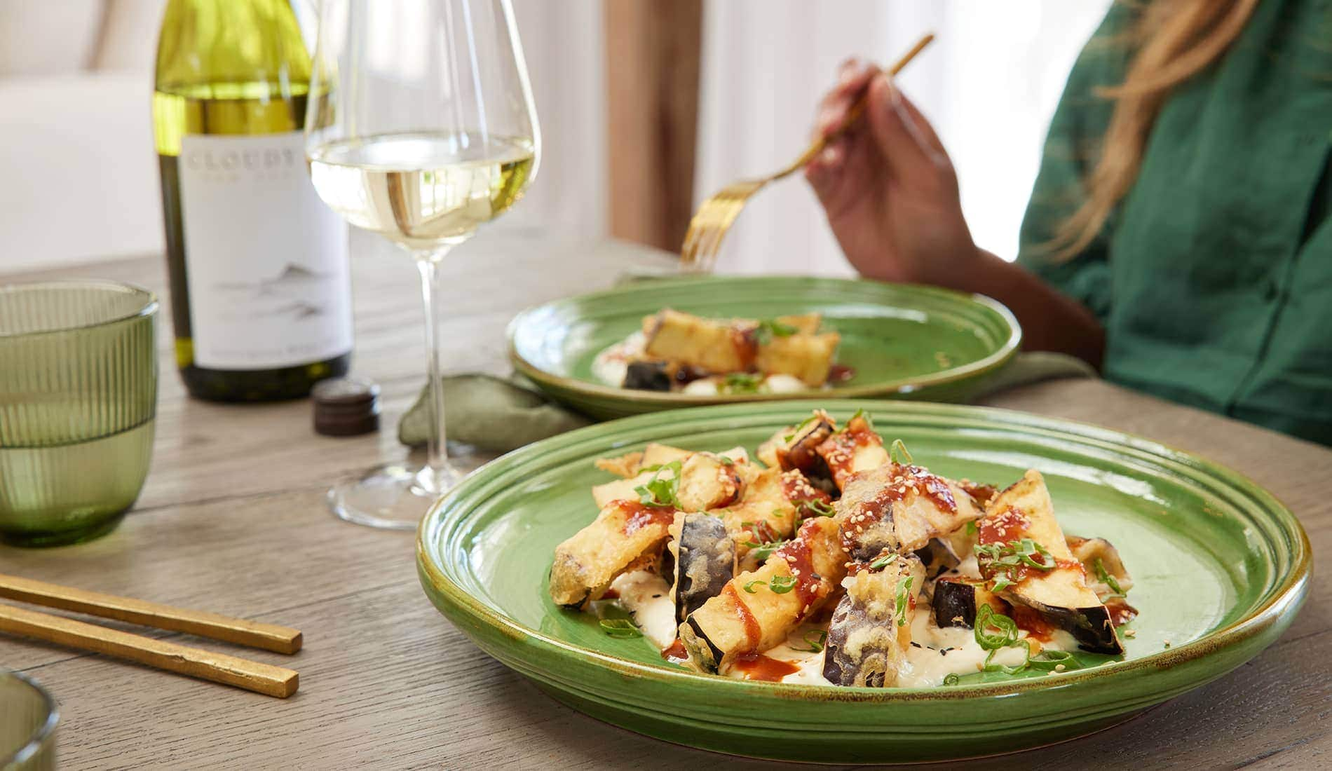 Two plates of food and a glass of white wine in front of a person and a bottle of Cloudy Bay wine