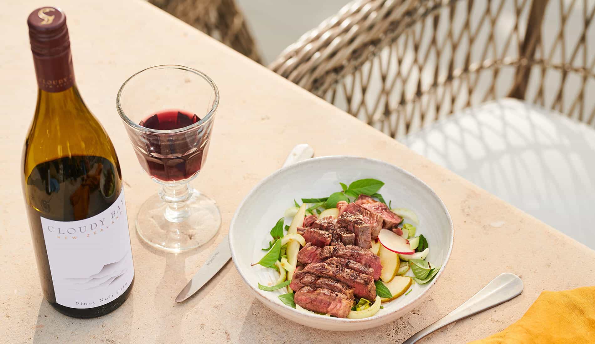 Plate of food beside bottle and glass of Cloudy Bay Pinot Noir