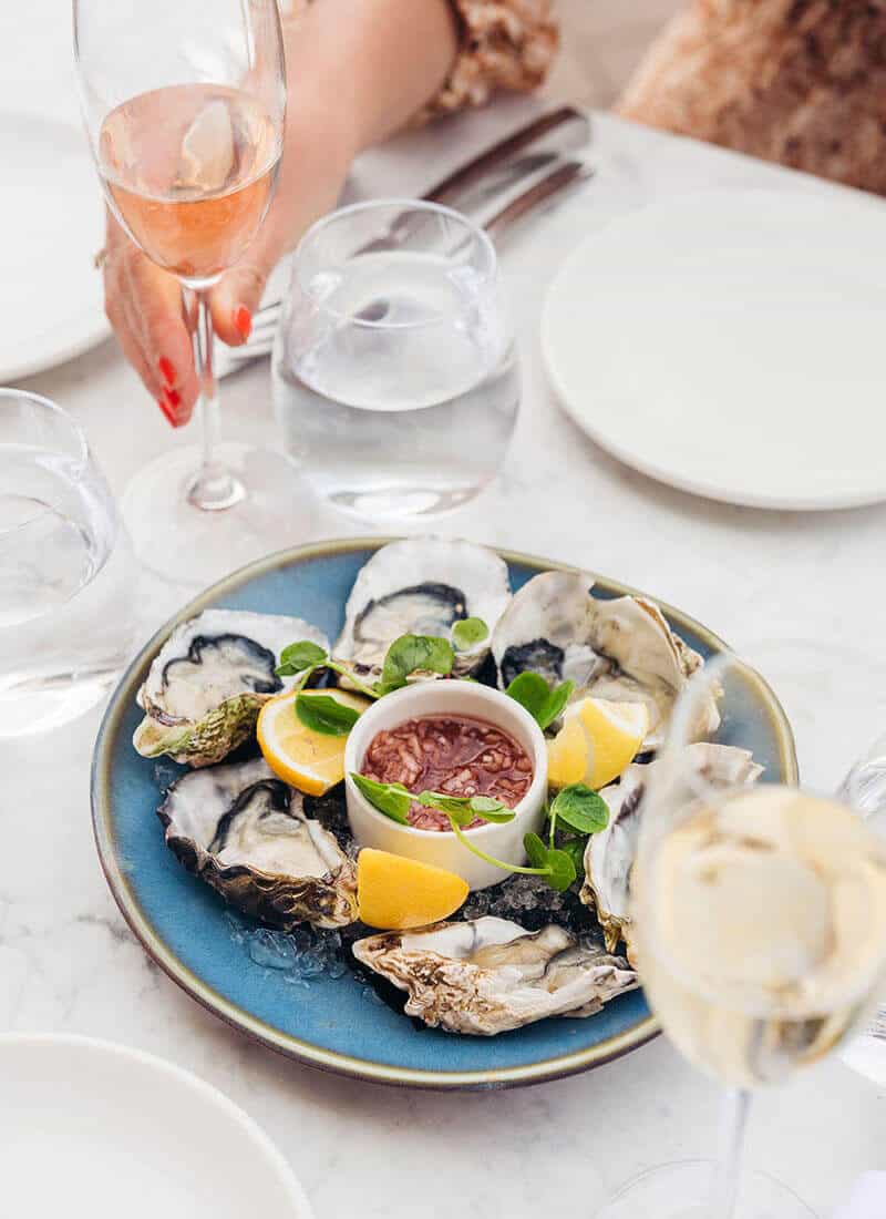 Plate of shucked oysters beside a hand holding a glass of sparkling wine