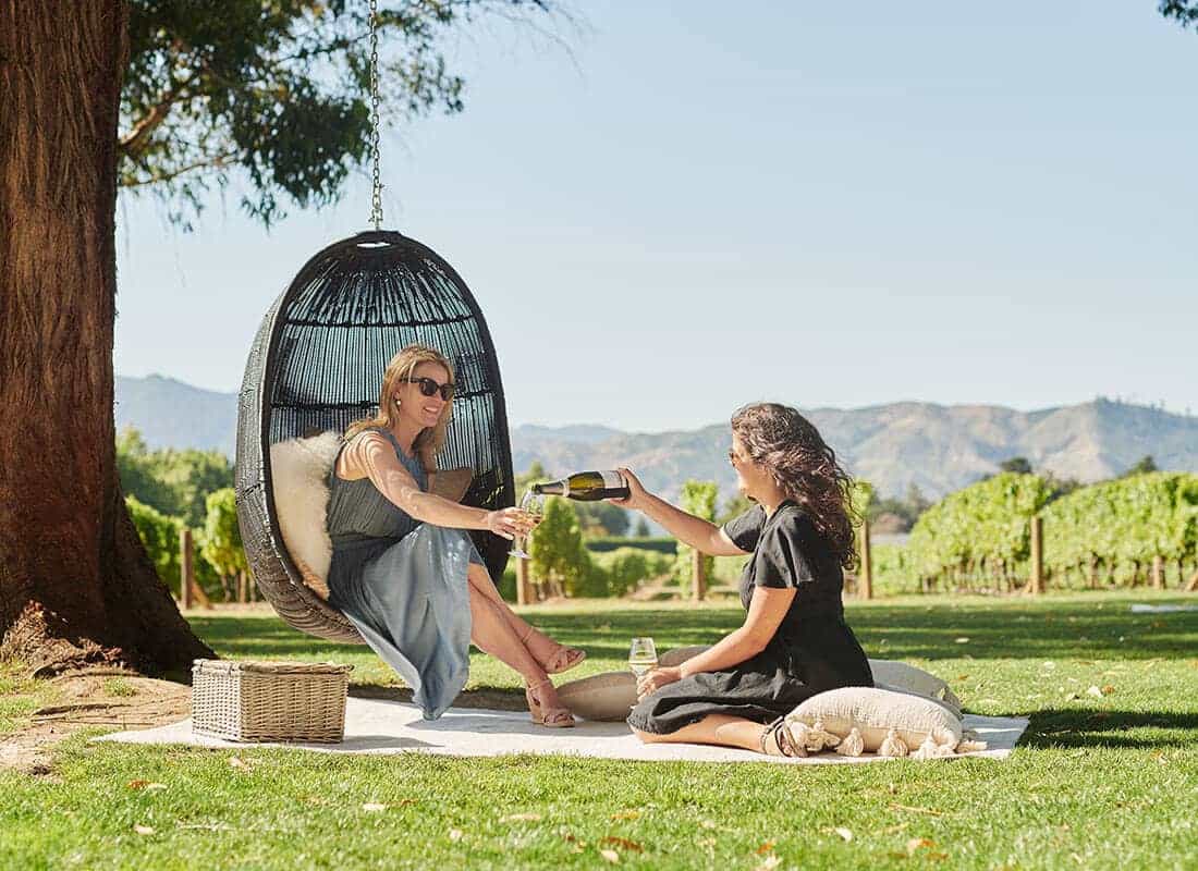 Two women sitting on a picnic mat, one pouring wine into a glass