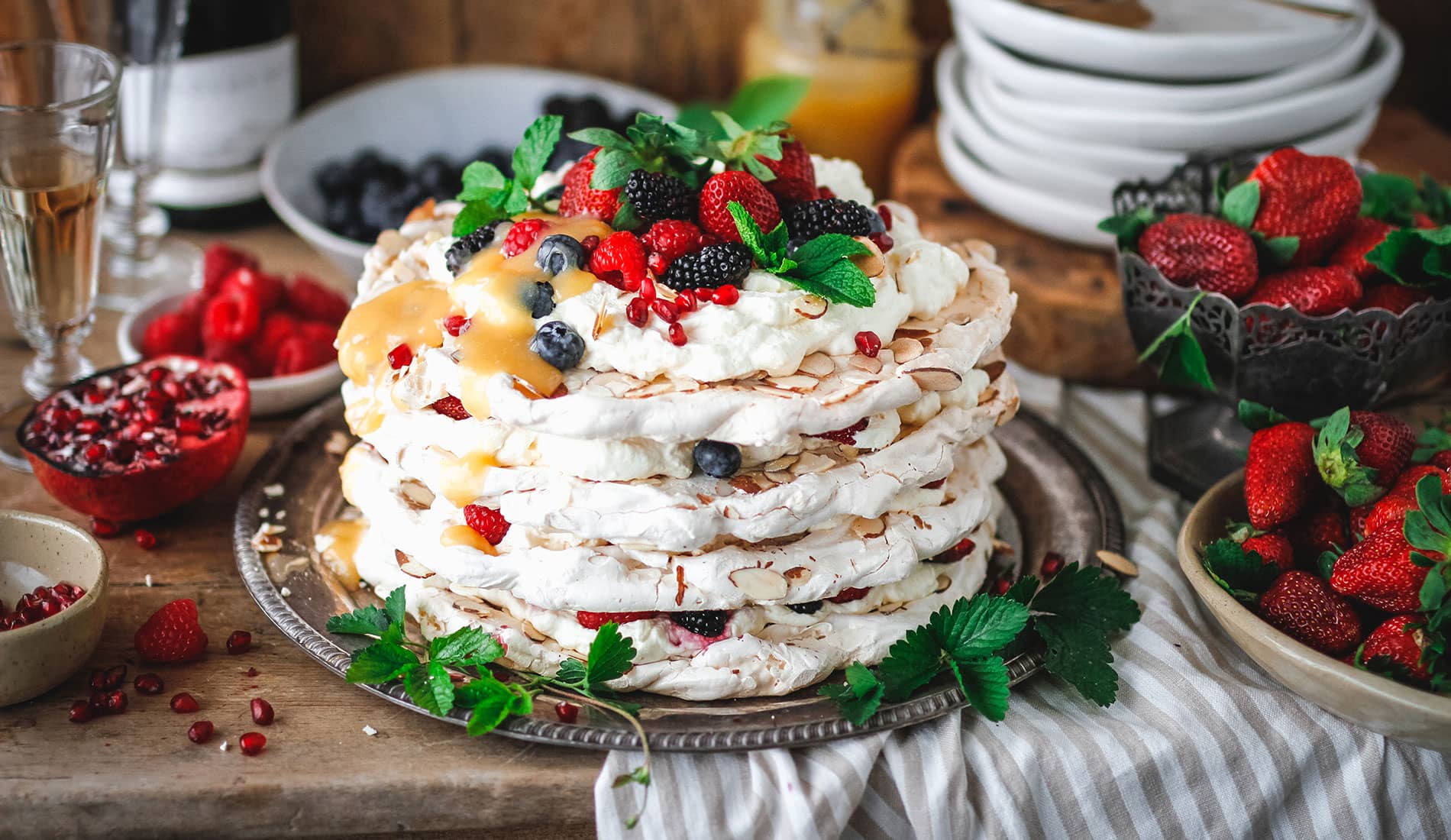 A layered meringue cake with fresh fruit and flaked almonds, and a bottle of Cloudy Bay Pelorus sparkling wine.