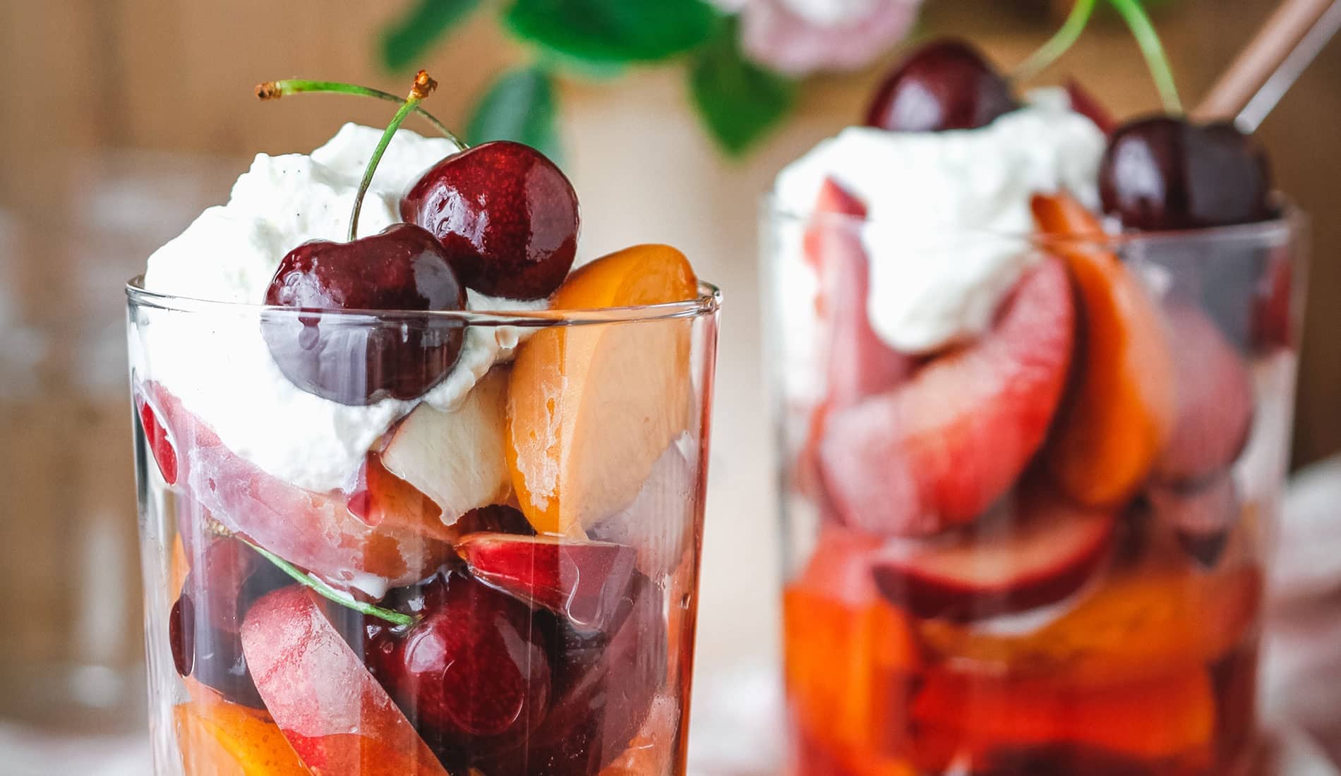 Two glass cups full of fresh fruit and cream