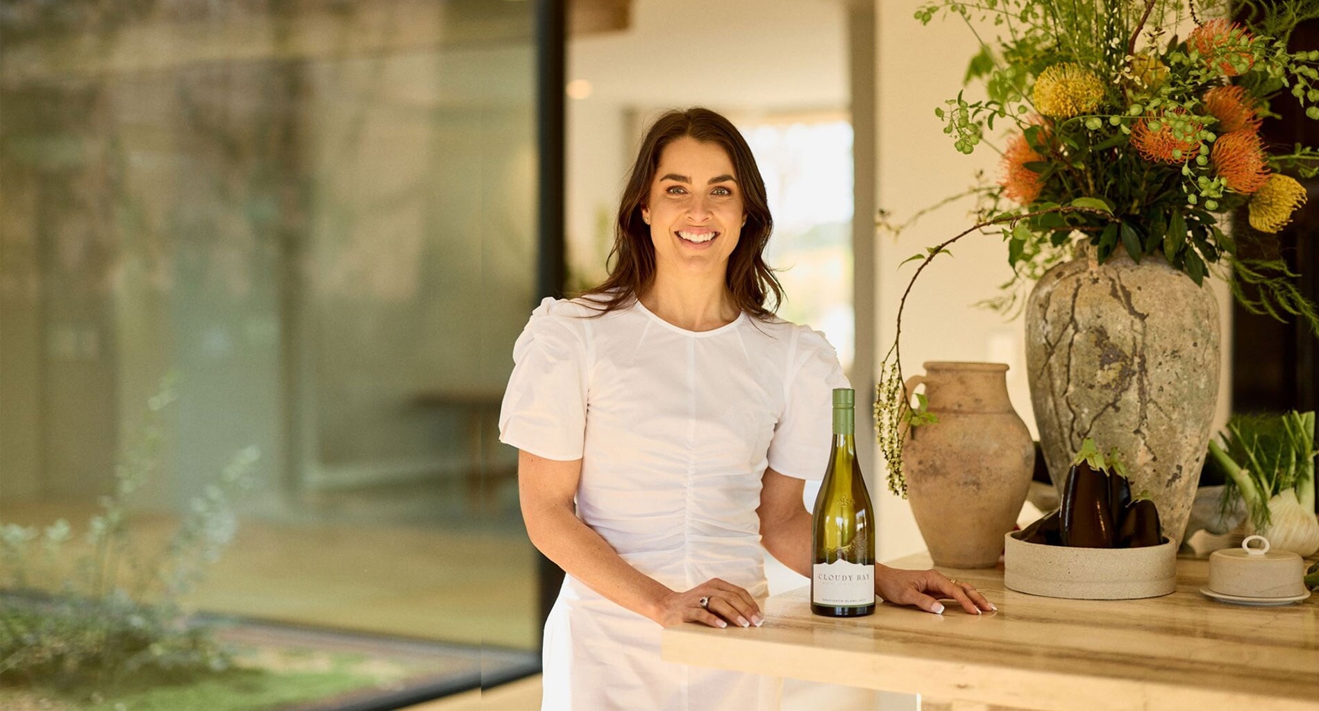 Desktop banner image showing Polly Markus with a bottle of Cloudy Bay Sauvignon Blanc 2023