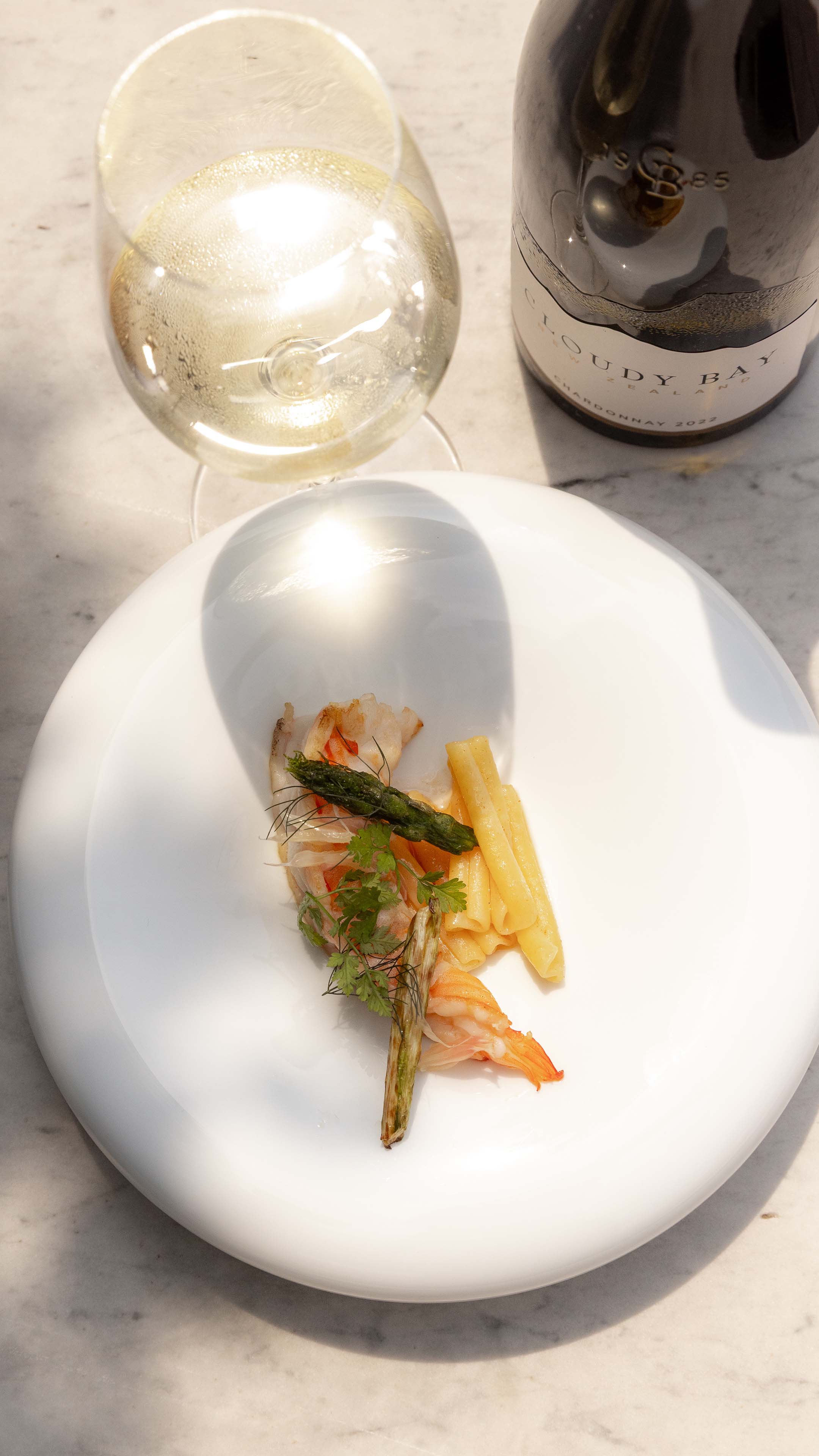 Close Up of Pan Seared Prawns with a glass and bottle of Cloudy Bay Chardonnay