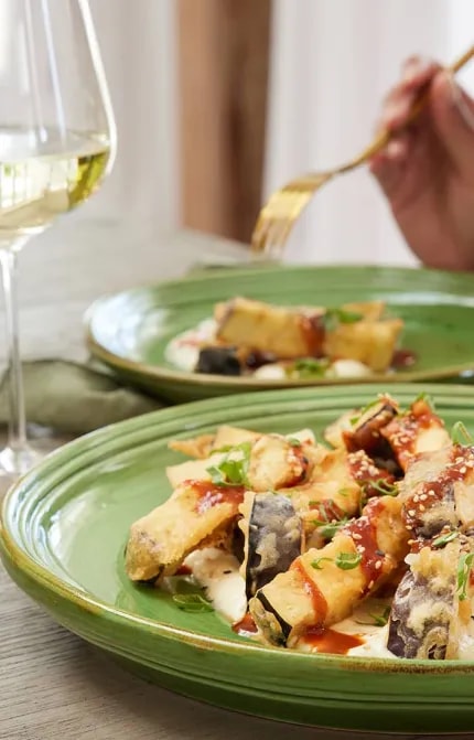 Two plates of food and a glass of white wine in front of a person and a bottle of Cloudy Bay wine