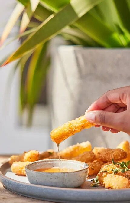 Hand holding croquette beside glass of white wine 