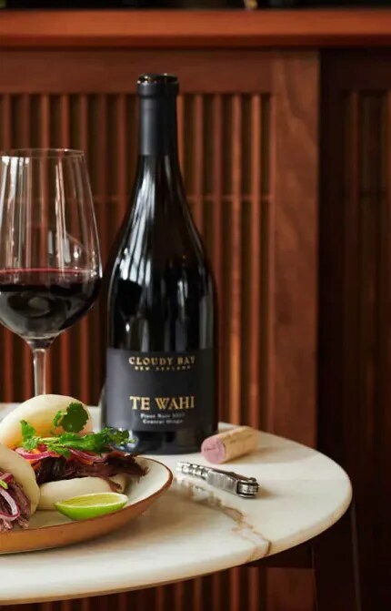 Bottle and glass of Cloudy Bay Te Wahi Pinot Noir beside plate of food